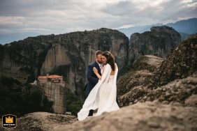 At Meteora, Greece, the couple shares an intimate pose atop a dramatic summit, with massive ancient boulders stretching out behind them, capturing breathtaking scenery and the feeling of togetherness in this iconic landscape.